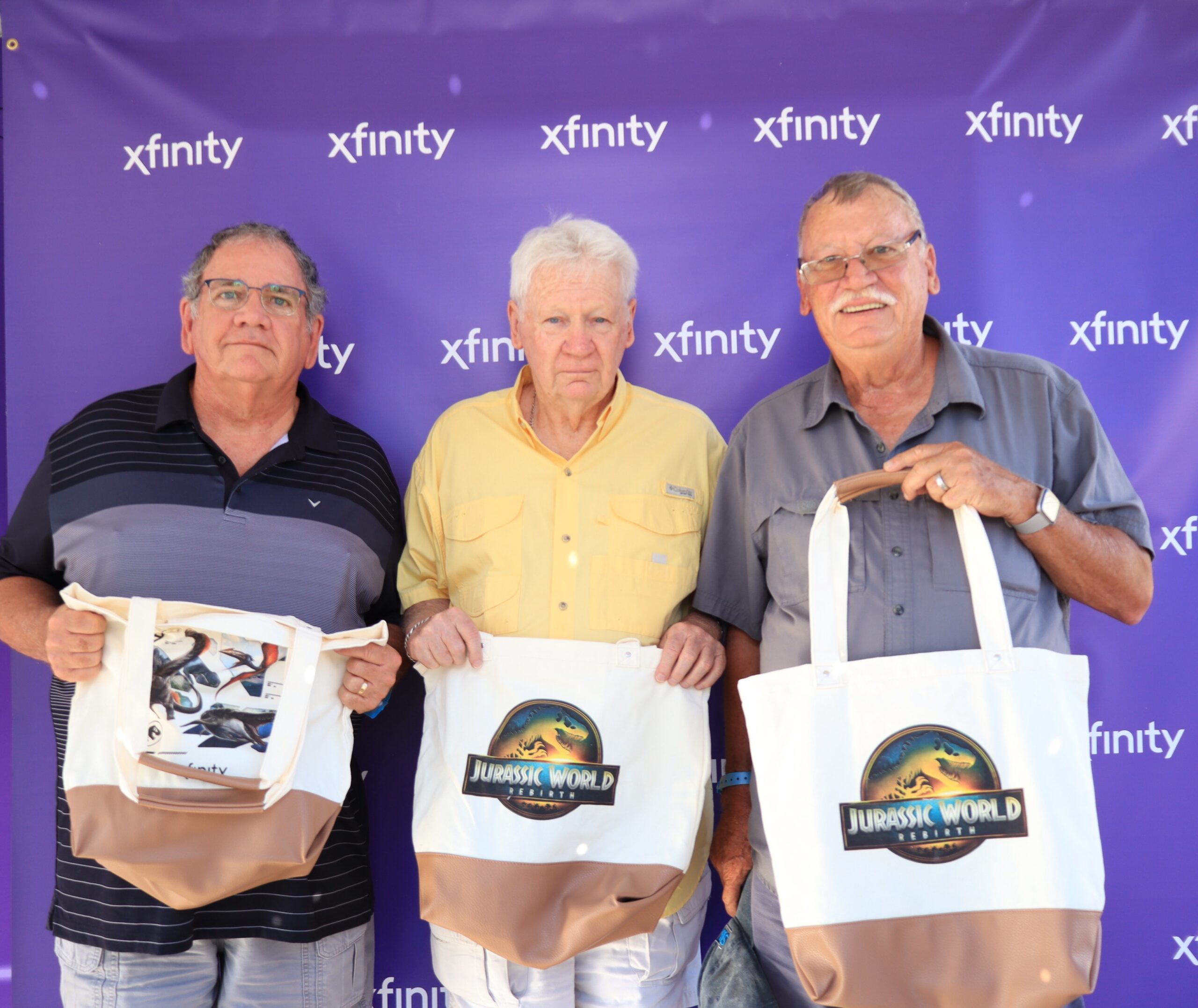 Three older men posing with Jurassic Park merch at Xfinity event