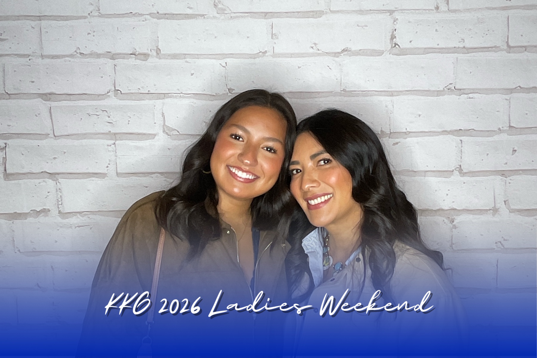 Two women posing together in front of a brick wall