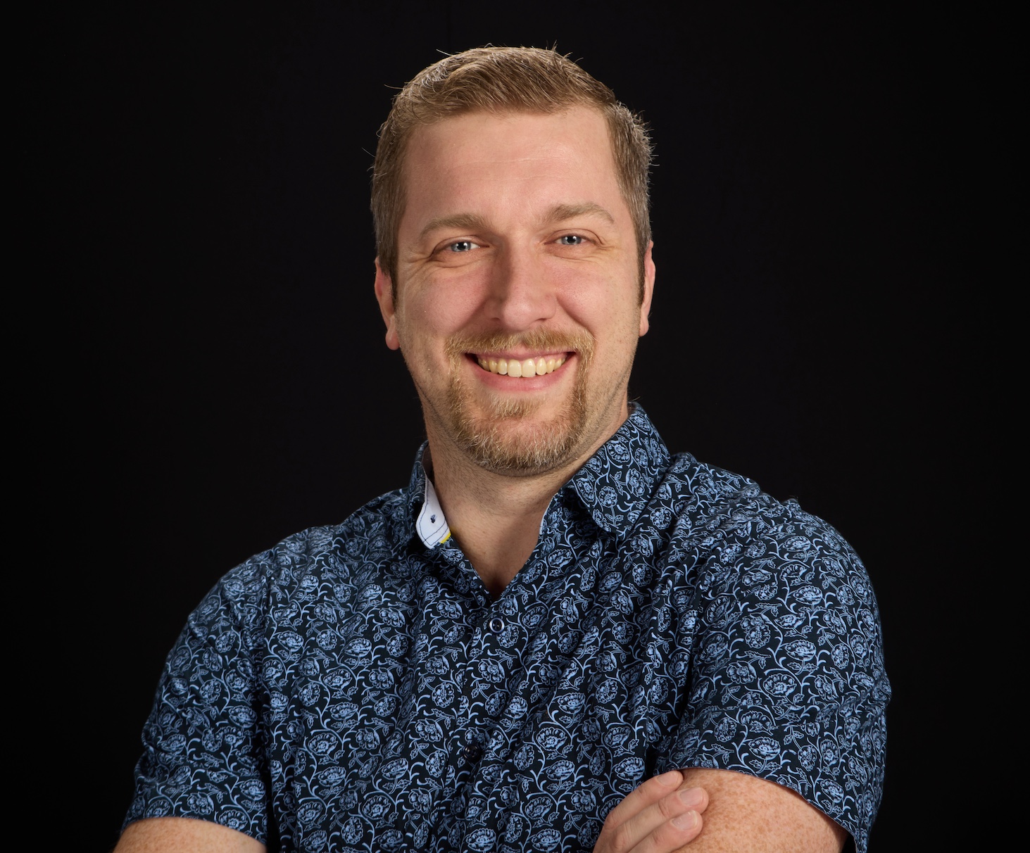 Man with a beard smiling in a patterned shirt 